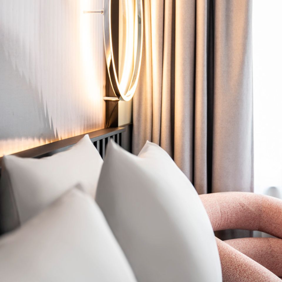 Bed with white pillows beside a tall window.