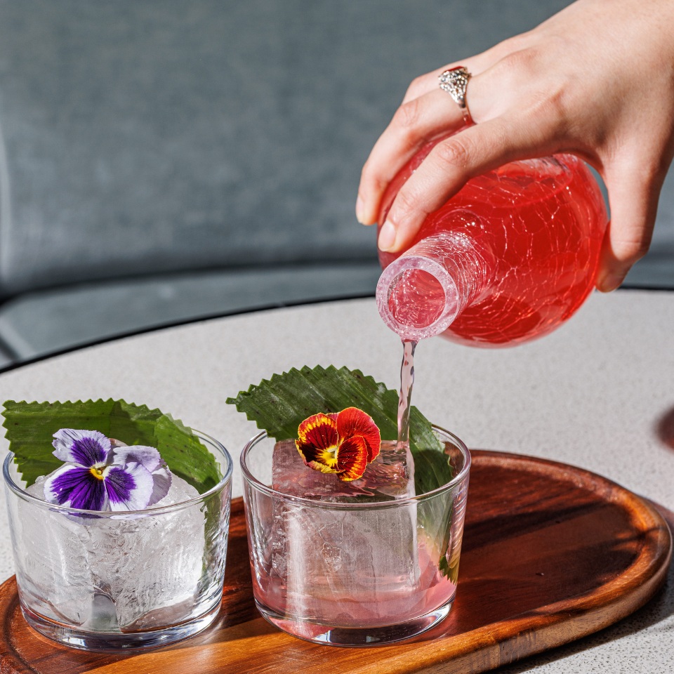 A person pours a red drink into glasses garnished with flowers.