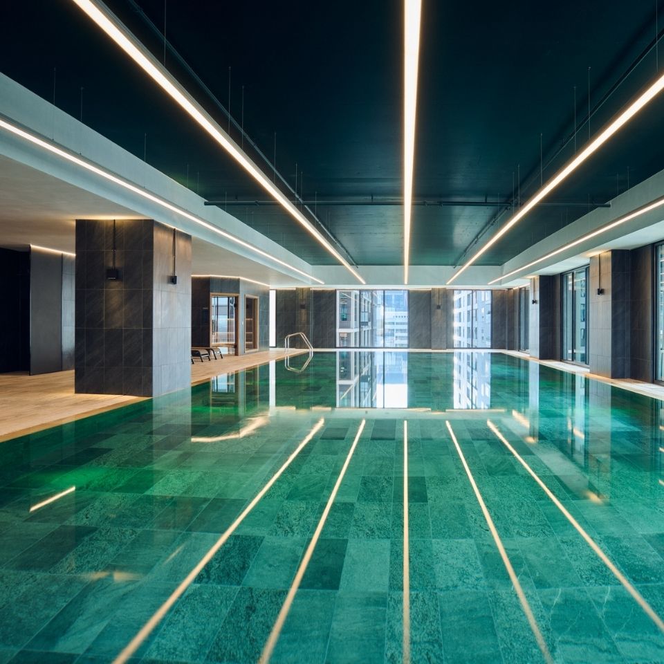 Indoor swimming pool beneath a dark ceiling with linear lights.