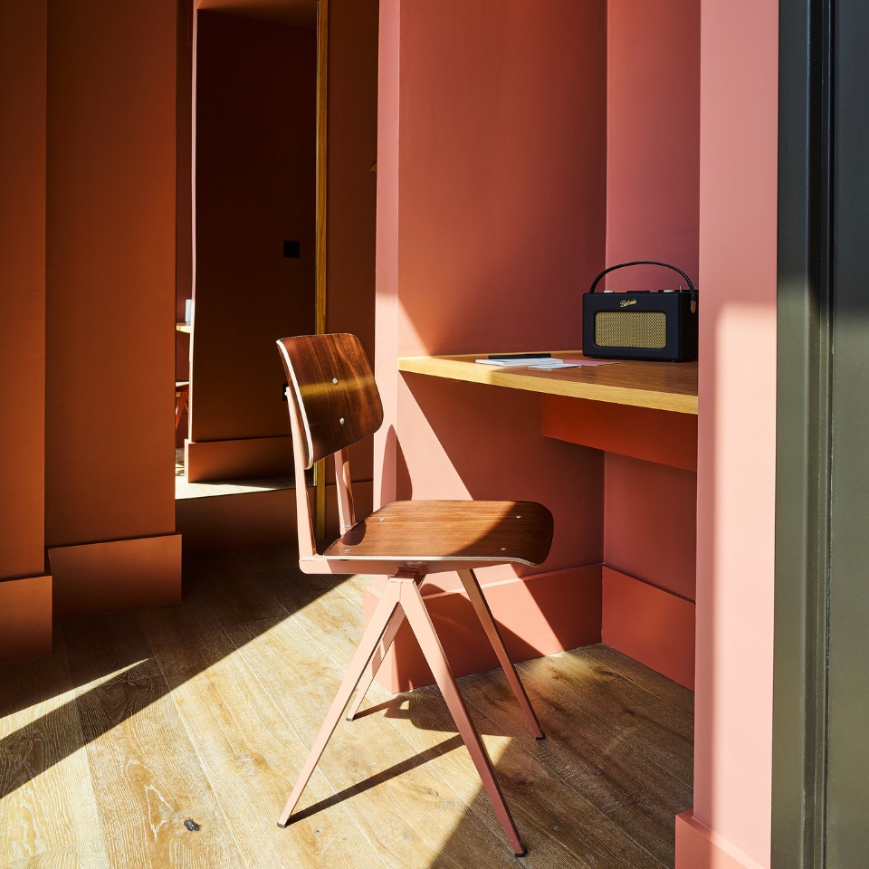Small desk and chair beside an open wardrobe and terracotta-coloured walls.