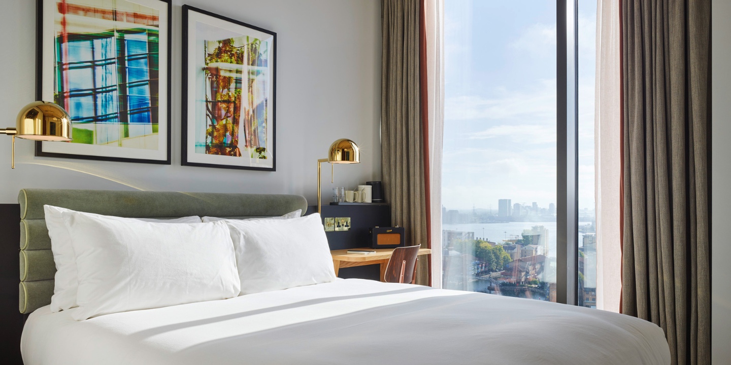 Double bed beneath framed artwork beside a window overlooking the city.