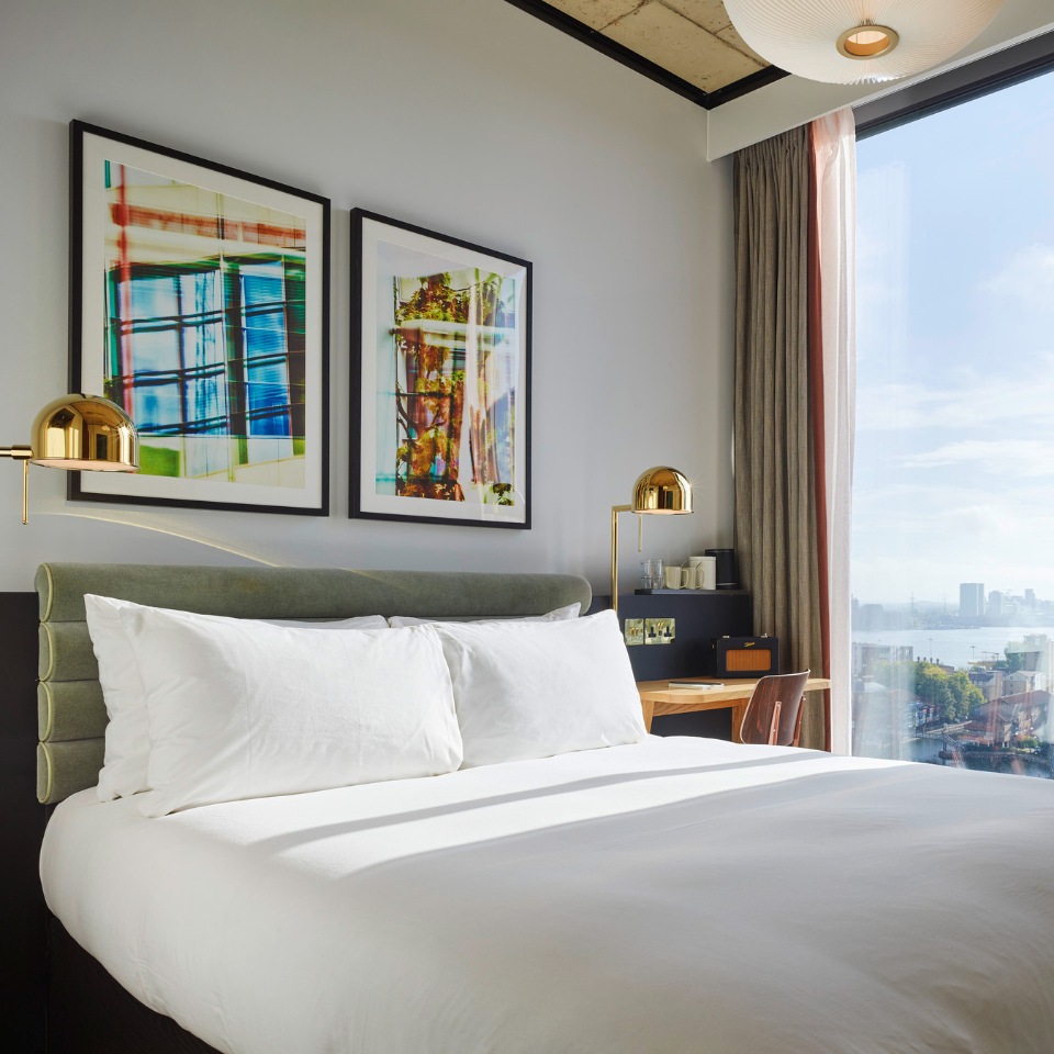 Double bed beneath framed artwork beside a window overlooking the city.
