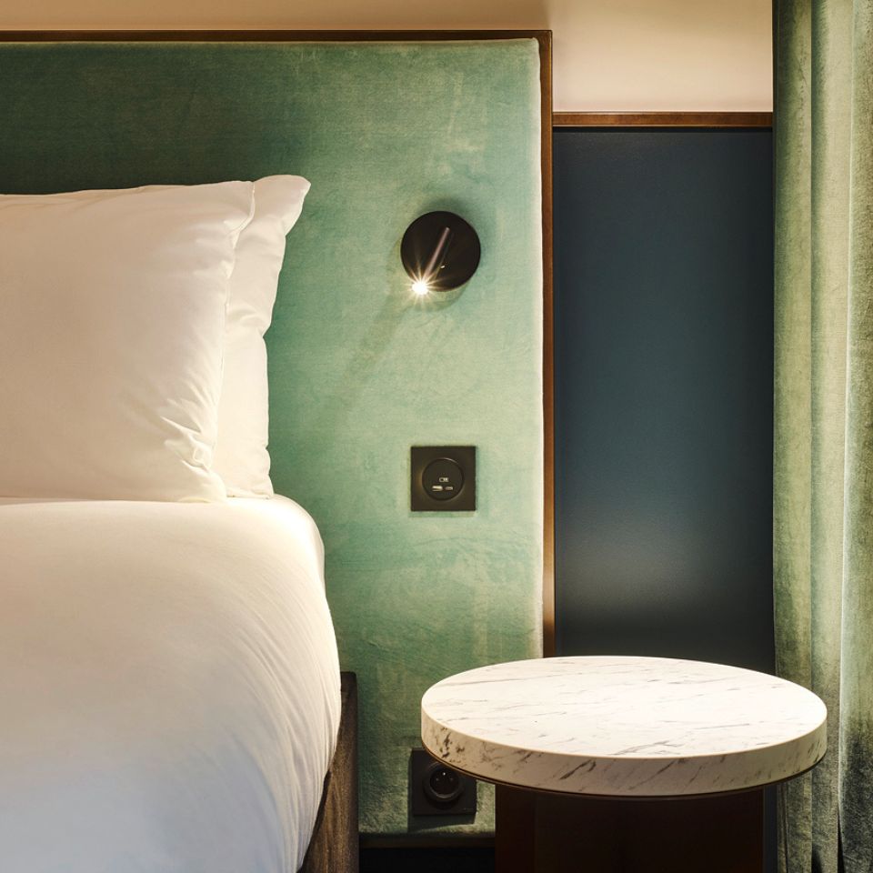 Bedside lamp and round table beside a green headboard.