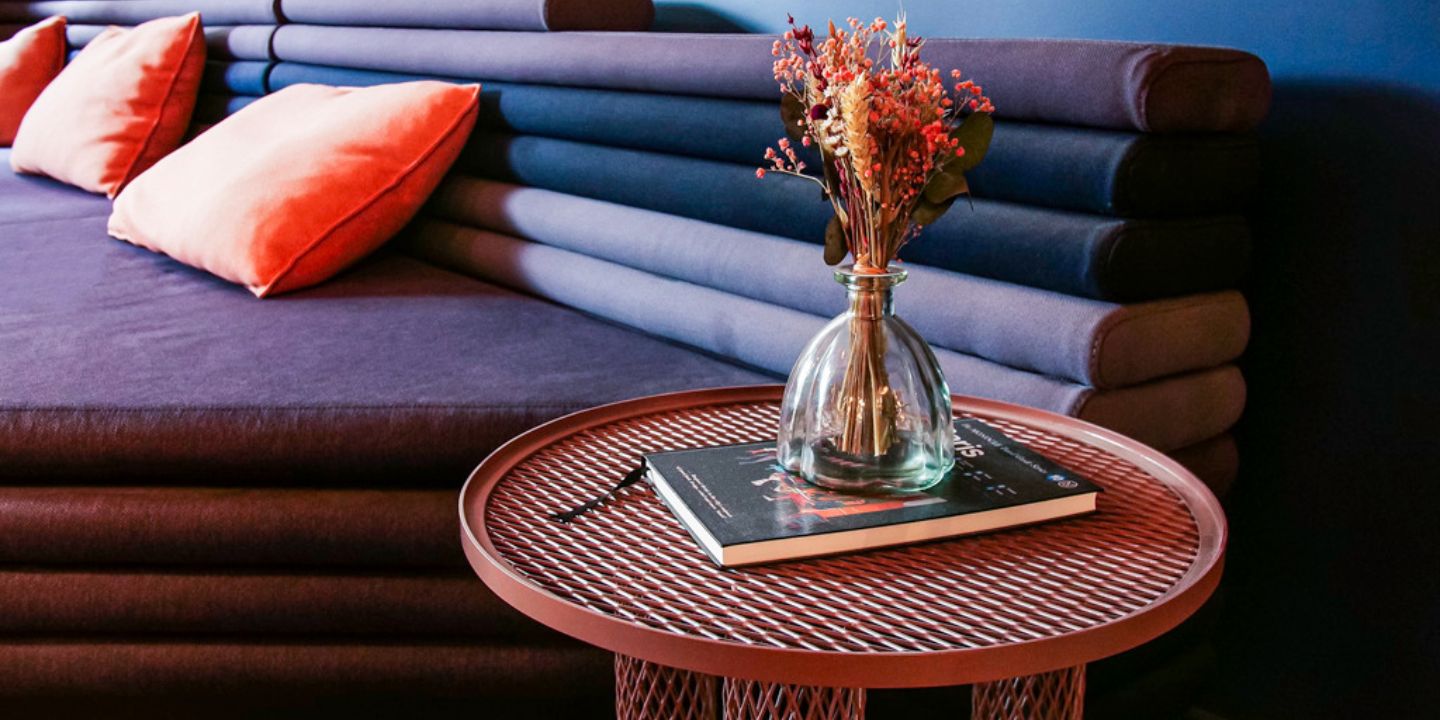 Table ronde avec fleurs près d’une banquette bleue aux coussins corail.