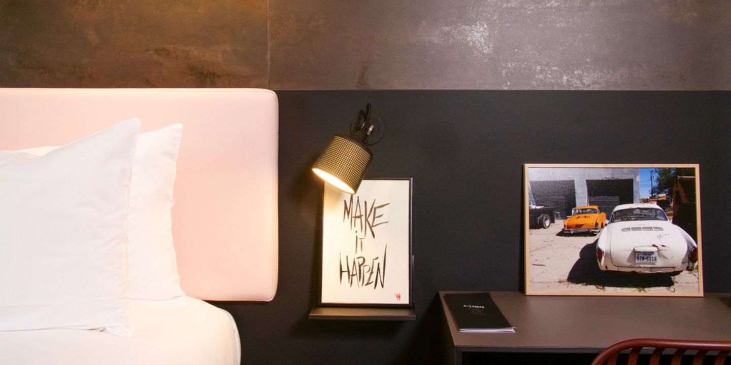 Lit à tête de lit rose avec lampe de chevet et œuvre encadrée.