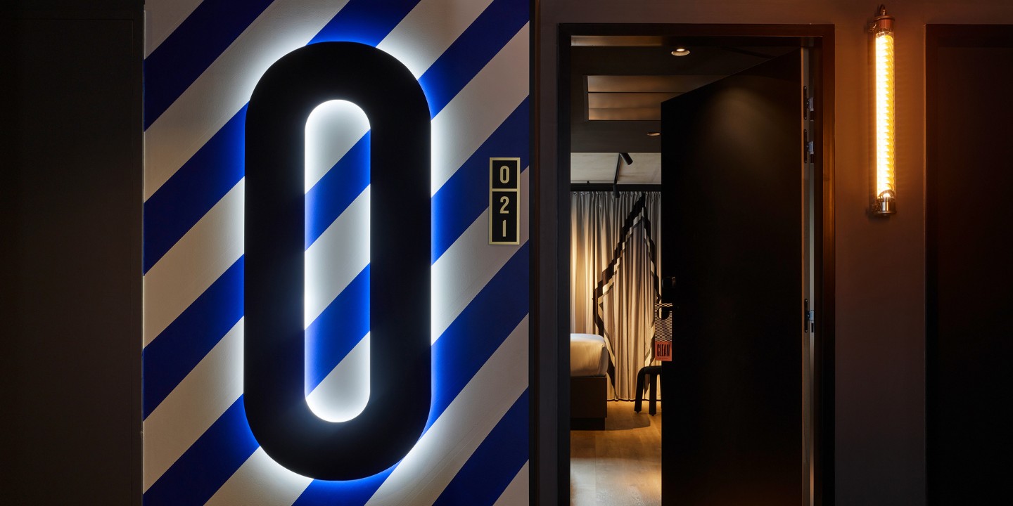 A black zero in front of a blue and white striped wall, it shows the floor number. in the background is an open door with a guest room