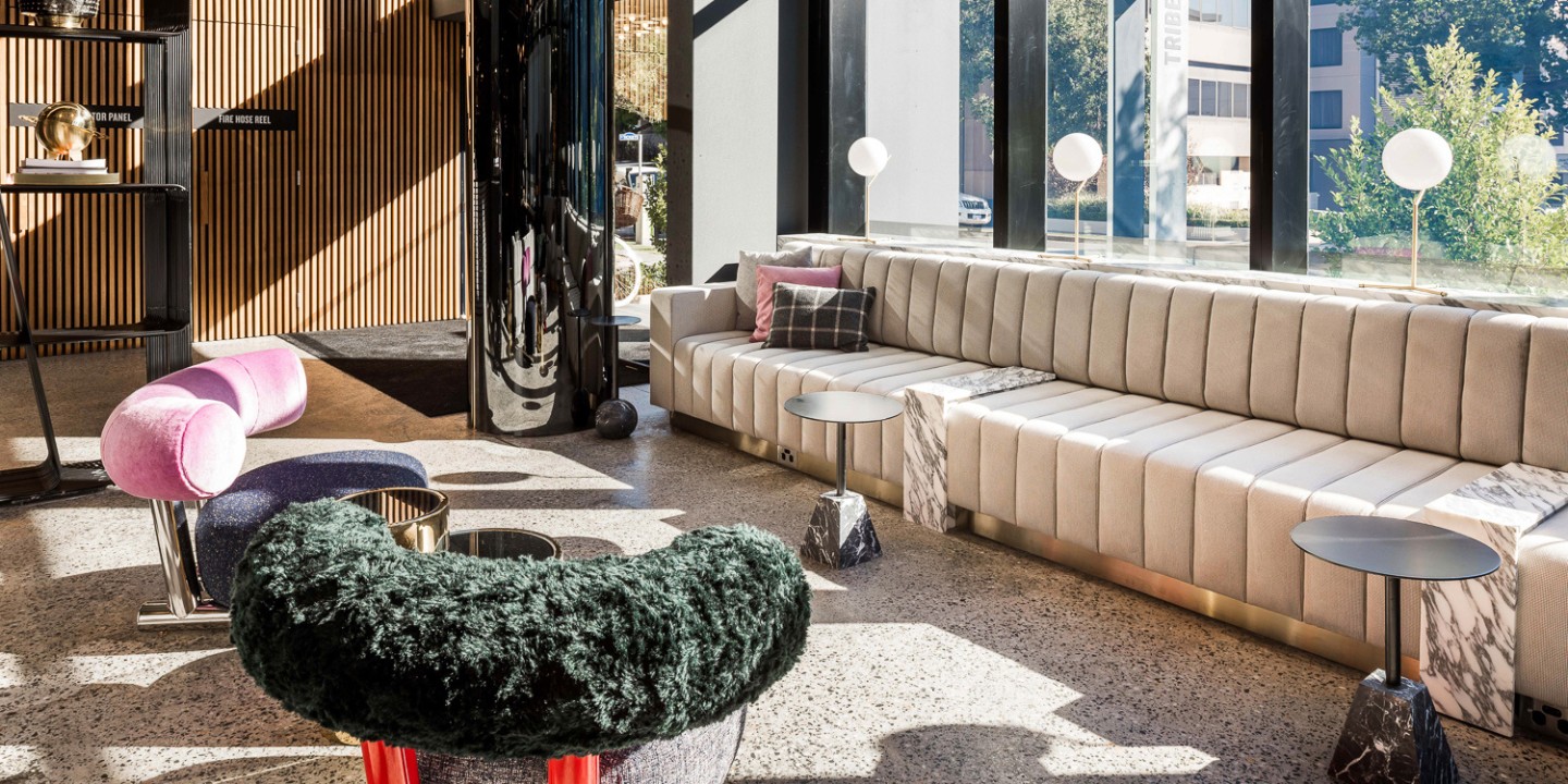 Large beige couch and colourful chairs with small, black tables.