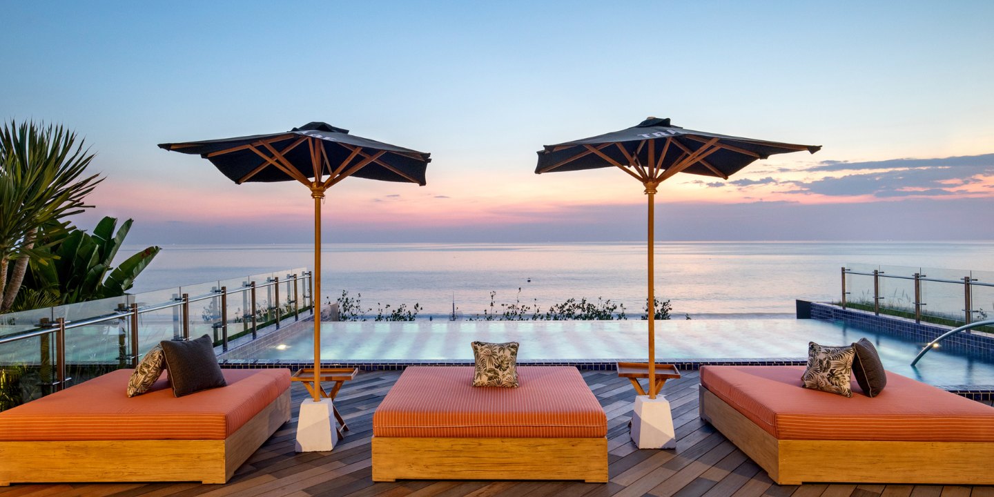 A rooftop pool and orange lounges with pillows on it