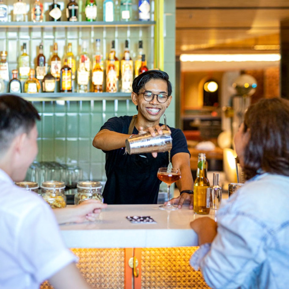 A bartender is pouring a drink for two guests sitting at the counter