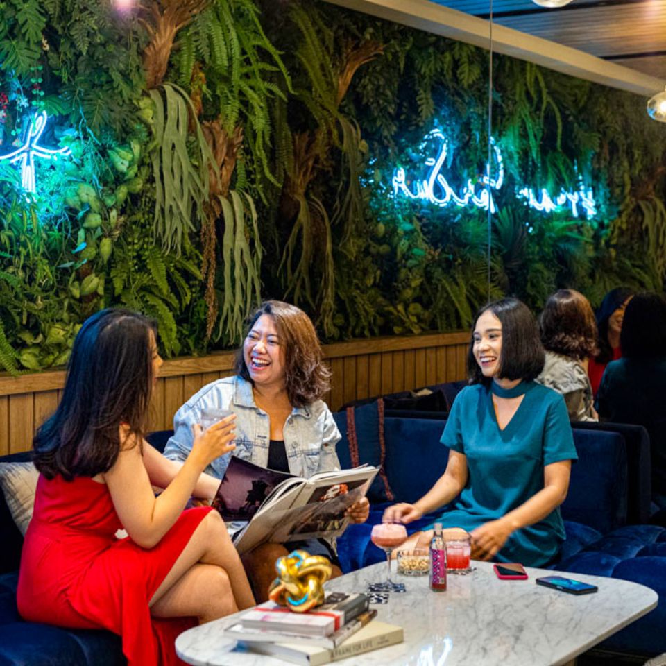 A group of people is sitting on cozy couches they are looking at magazines while talking