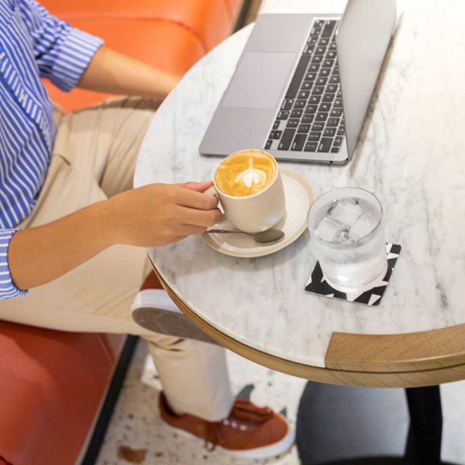 A person works at a laptop over coffee.