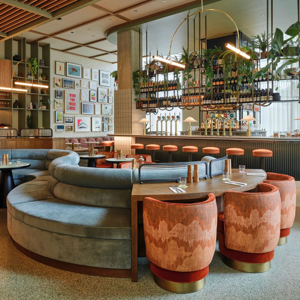 A large round couch and tables with chairs, in the background is a bar