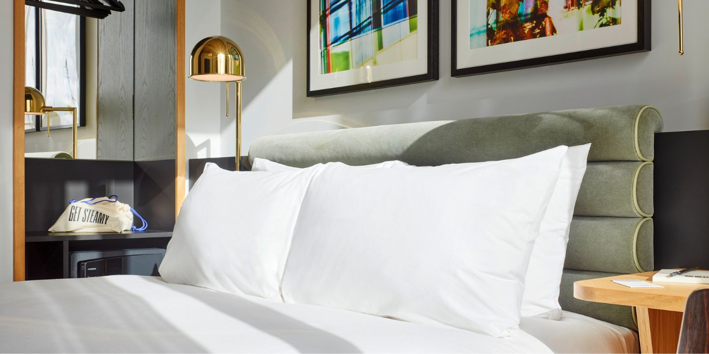 A close-up of a double bed with white linens and a green headboard