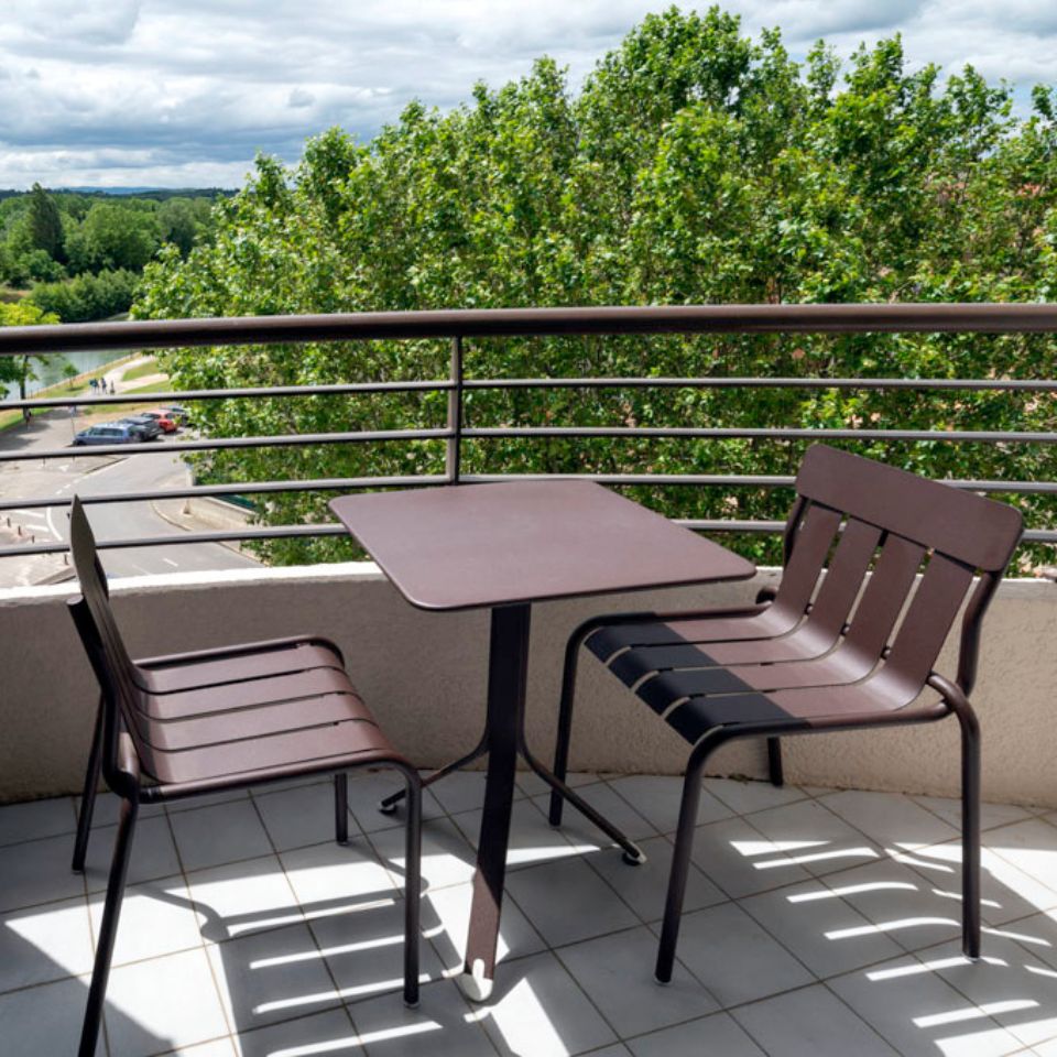 Table et chaises sur un balcon donnant sur les arbres.