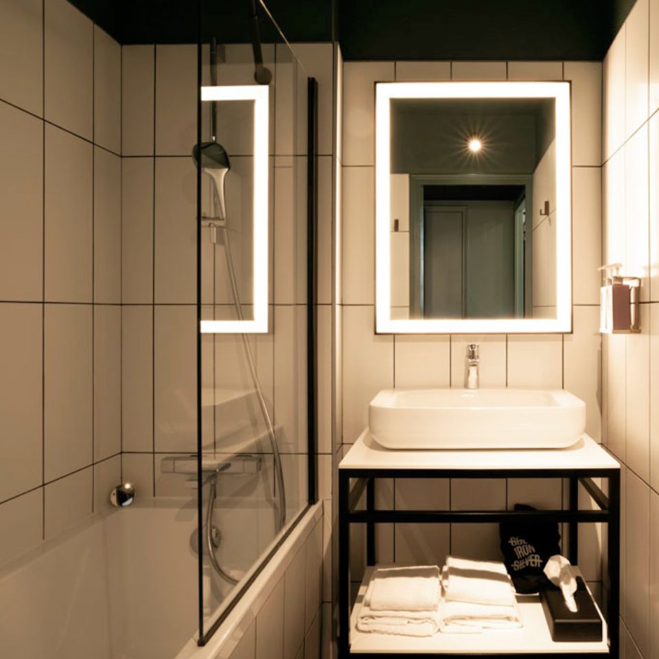 Salle de bains avec douche, baignoire, miroir éclairé, lavabo et serviettes pliées.