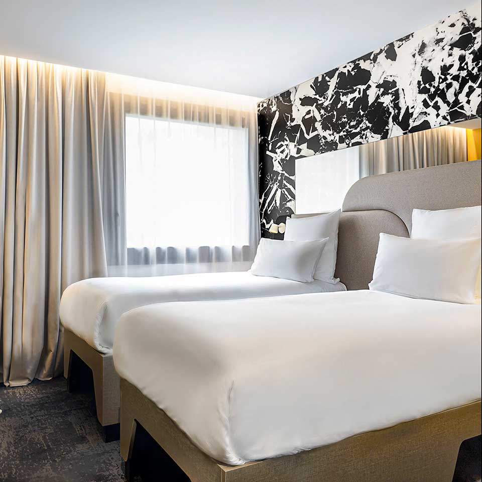 Hotel room with two single beds, window with curtains and marble patterned back wall