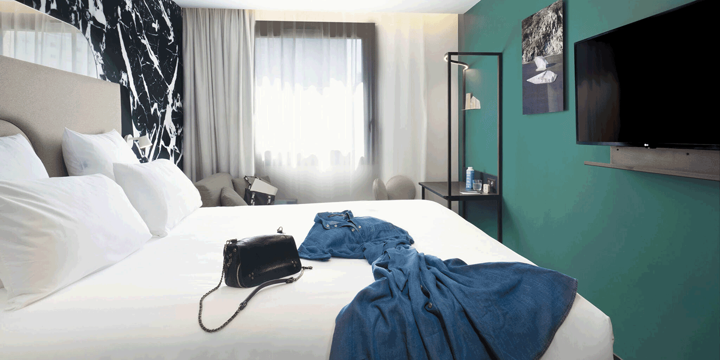 Hotel room with dress and handbag laying on double bed, sofa bed and small desk.