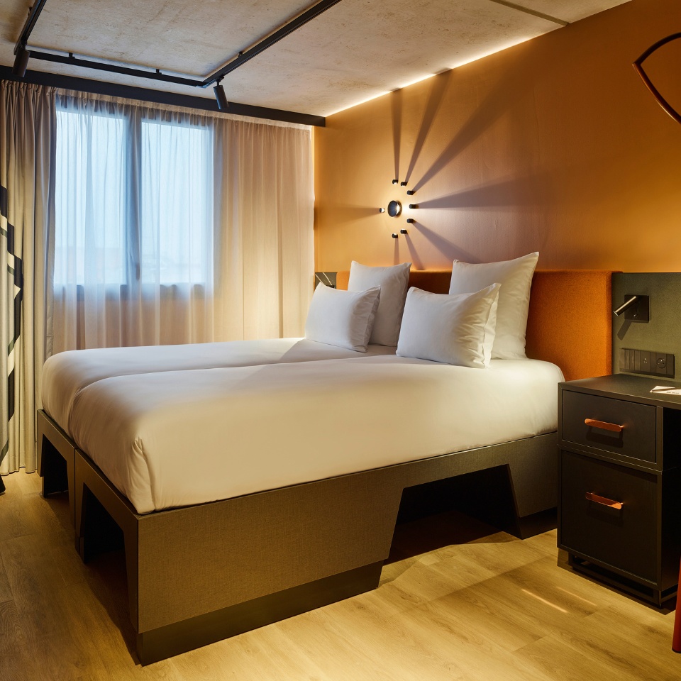 Double bed with an orange headboard and a black nightstand next to it, the curtains are drawn