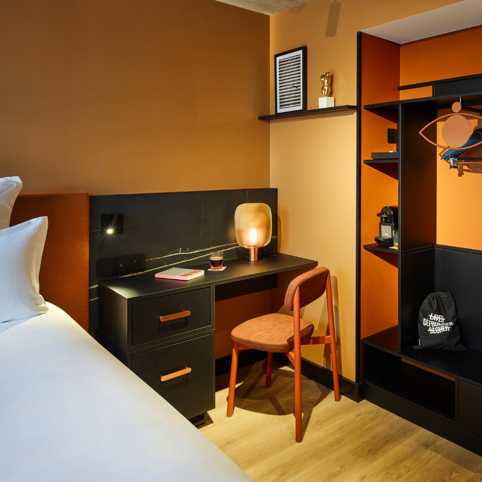A small black desk with an orange chair next to a hotel bed