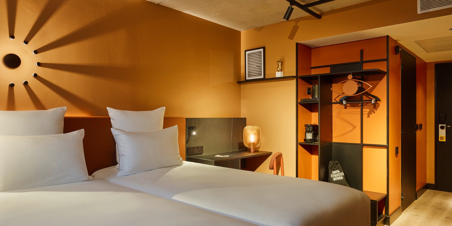 A twin bed with a small black desk next to it and an orange-black wardrobe