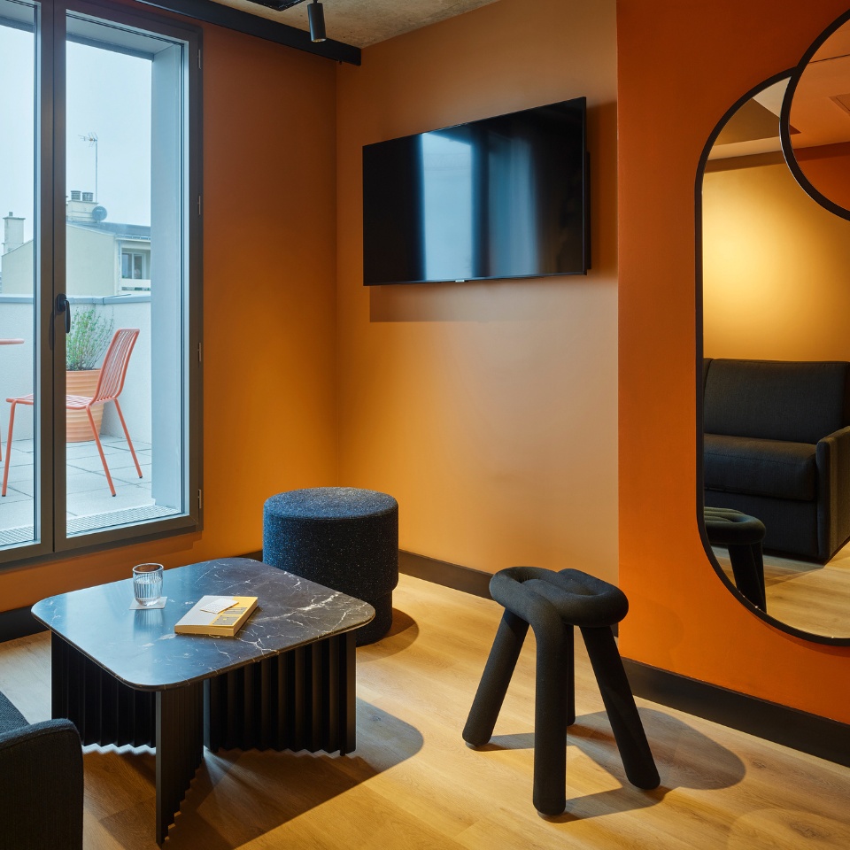 Living area in a hotel room with small black chairs and a couch and a marble coffeetable in front of a terrace door
