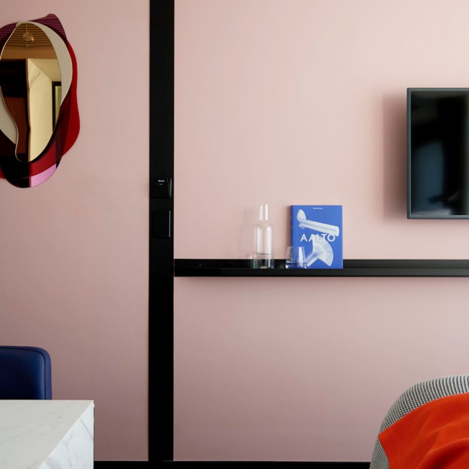 Bedroom with pink walls, mirror, shelf and television.
