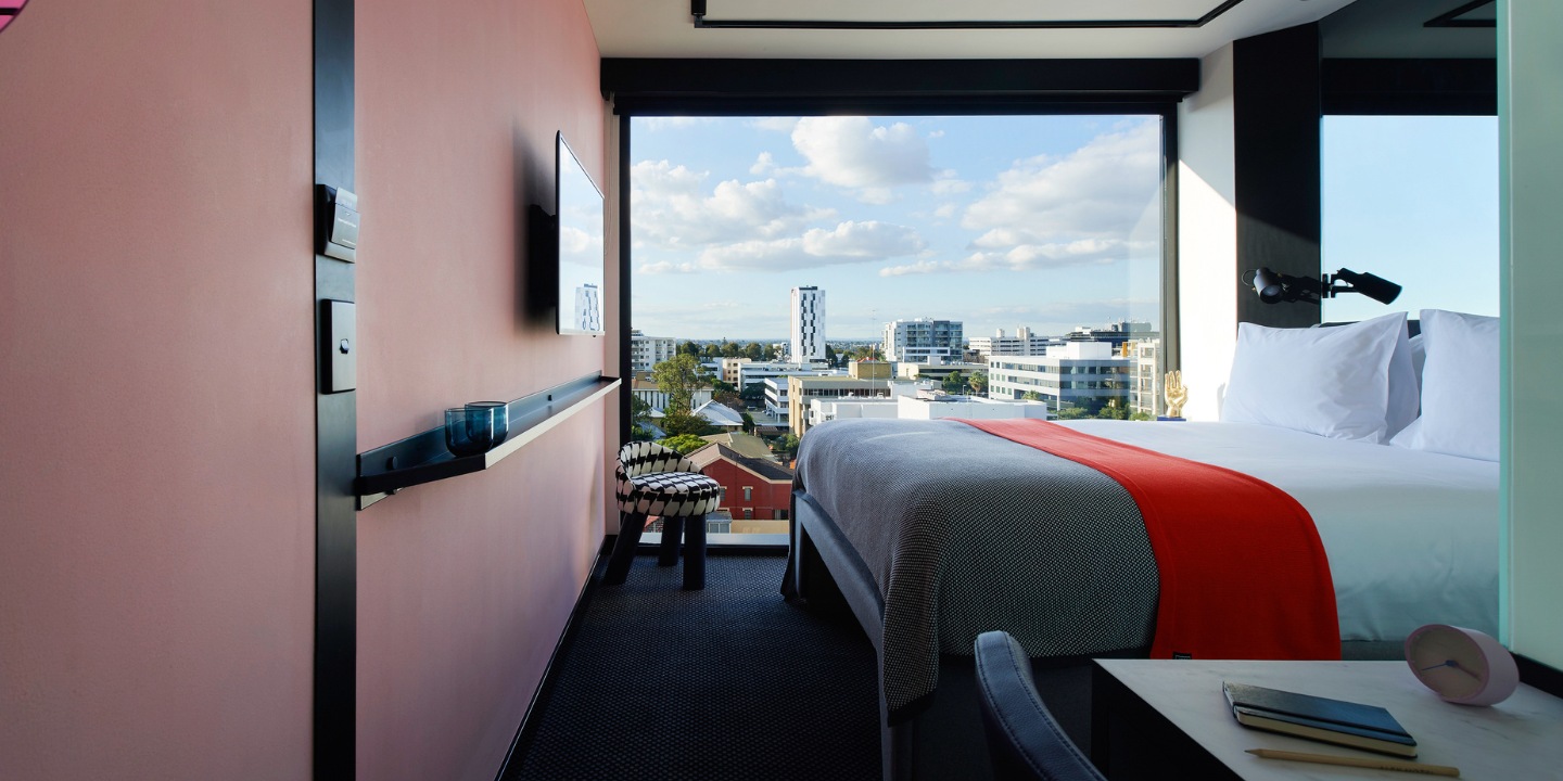 Bed and desk beside a large window with a city view.