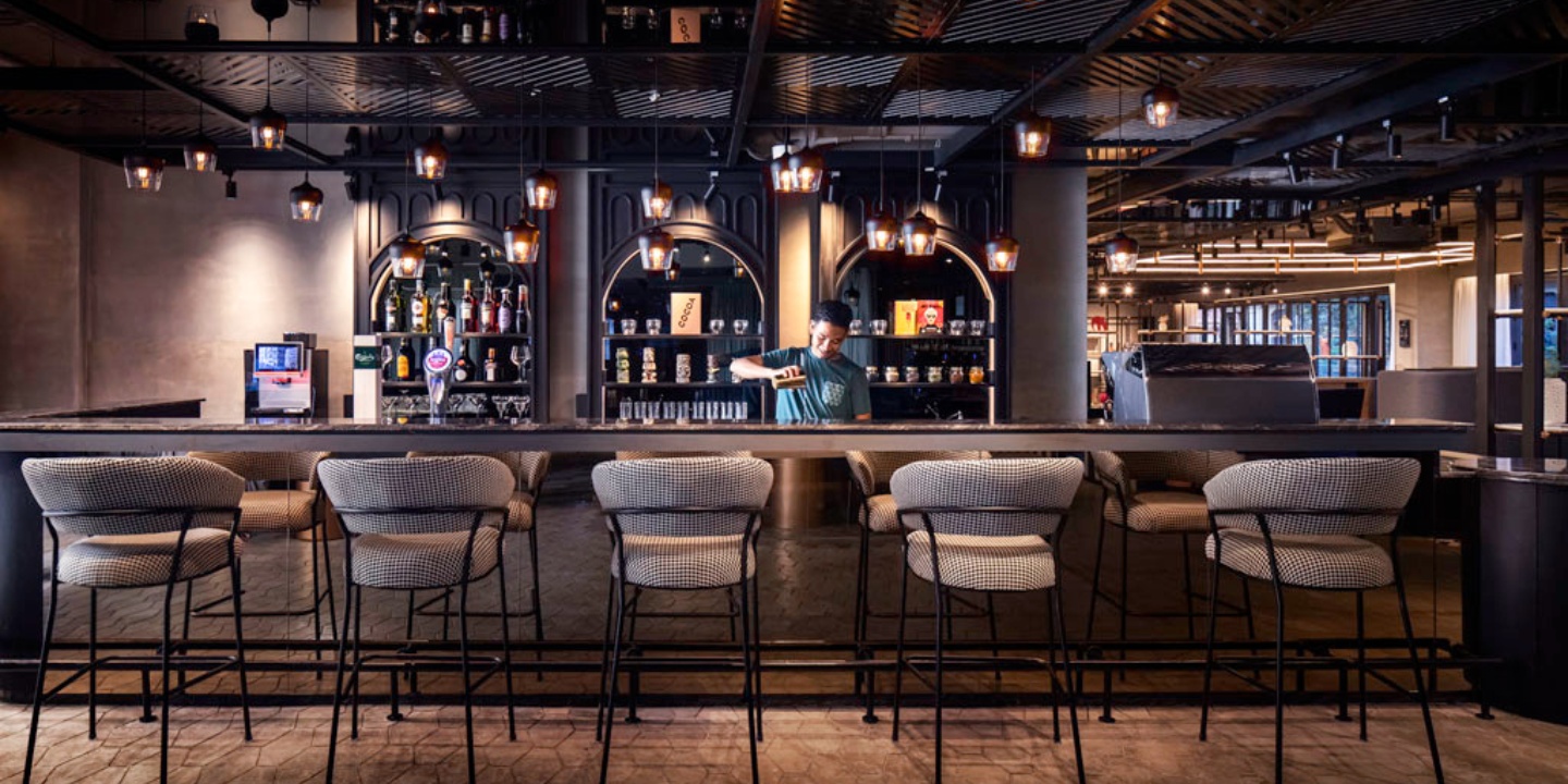 Le bar TRIBE Express, avec un barman qui sert une boisson derrière le comptoir et des chaises hautes devant ; plusieurs alcools en arrière-plan