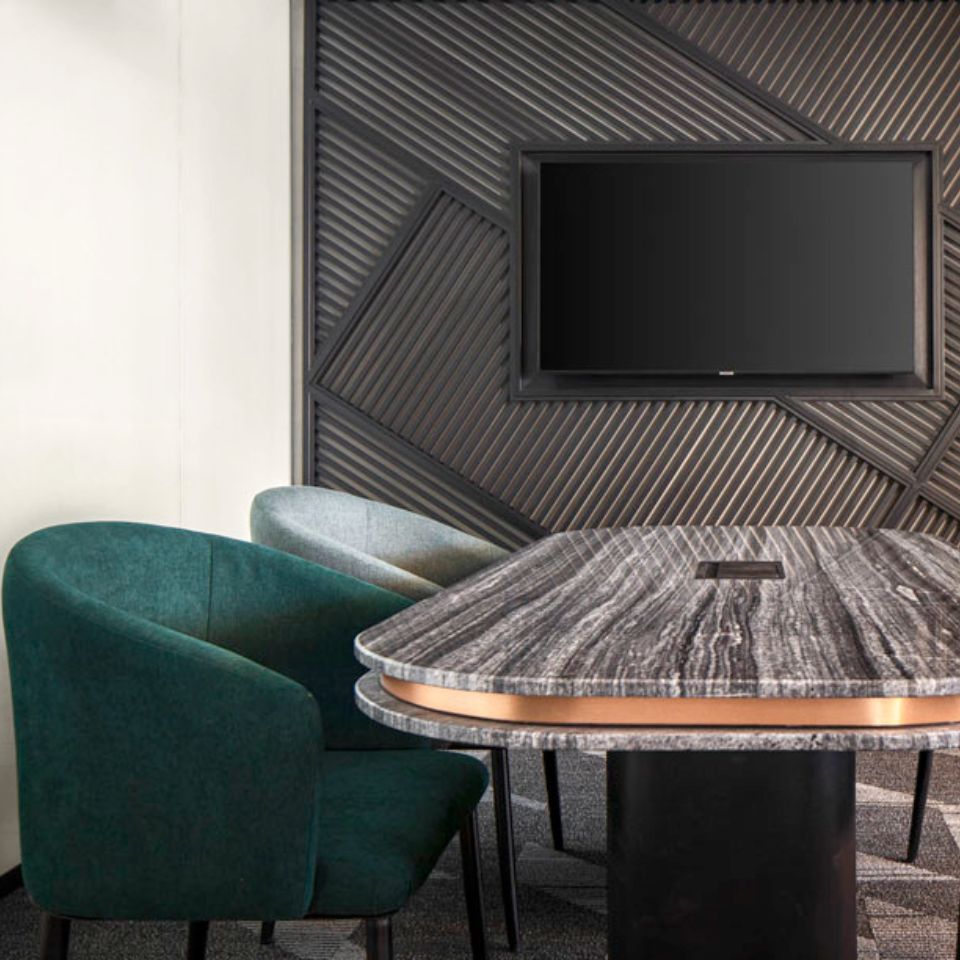Une salle de réunion avec une table en marbre au centre, deux chaises et une télévision murale.
