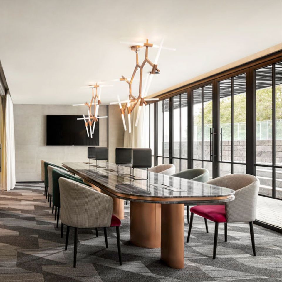 Fauteuils gris et verts autour d’une grande table dans un espace de coworking, à côté d’une baie vitrée du sol au plafond