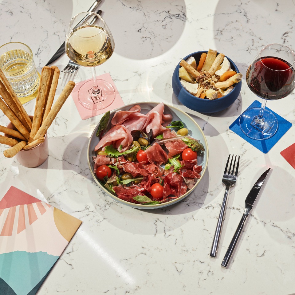 A table setting with a bowl of salad with ham and two glasses of wine, as well as several appetizers