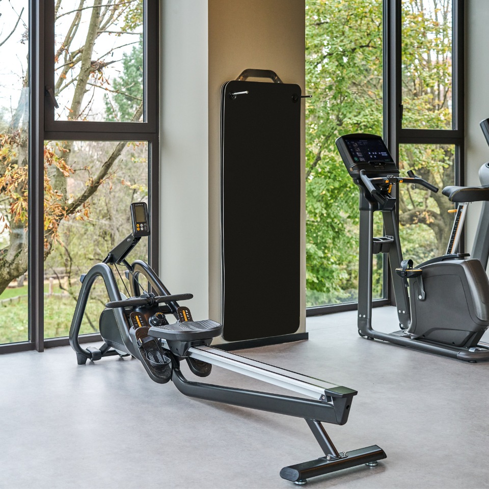 Wooden rowing machine and exercise equipment beside a large window.