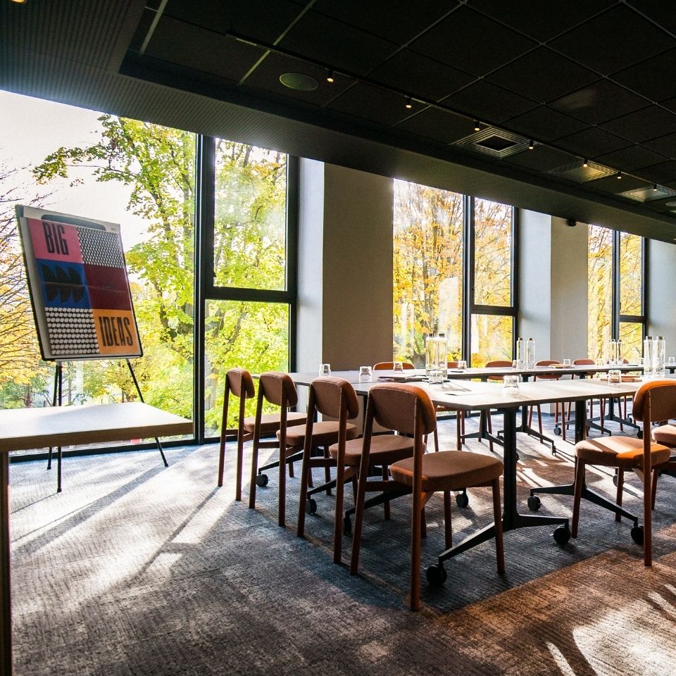 Meeting tables and chairs beside windows overlooking trees.