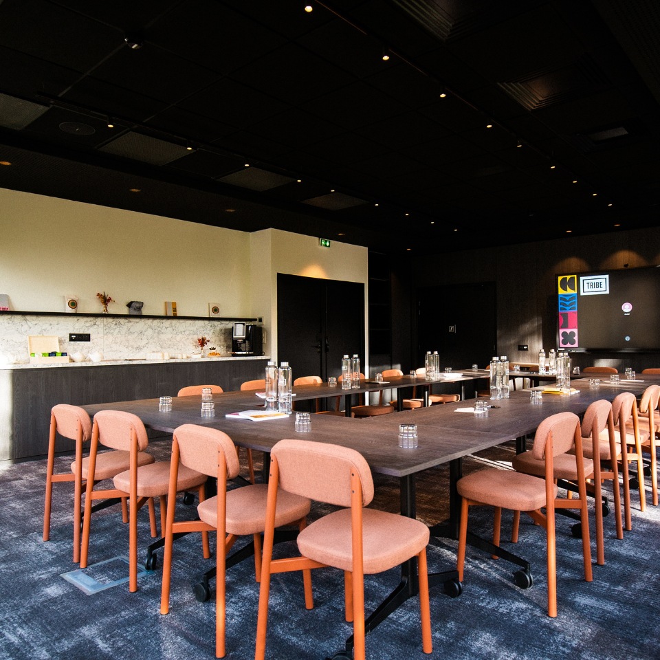 Long meeting table with orange chairs and water glasses.