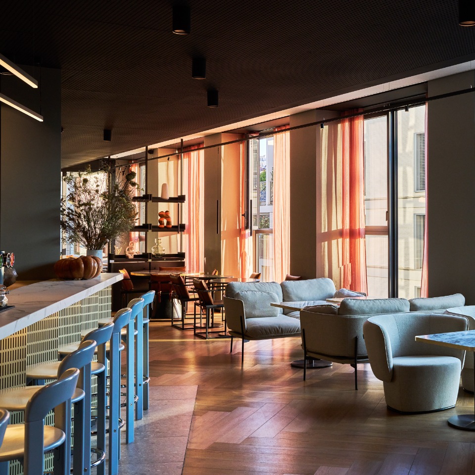 Long bar with blue stools and lounge seating beside tall windows.