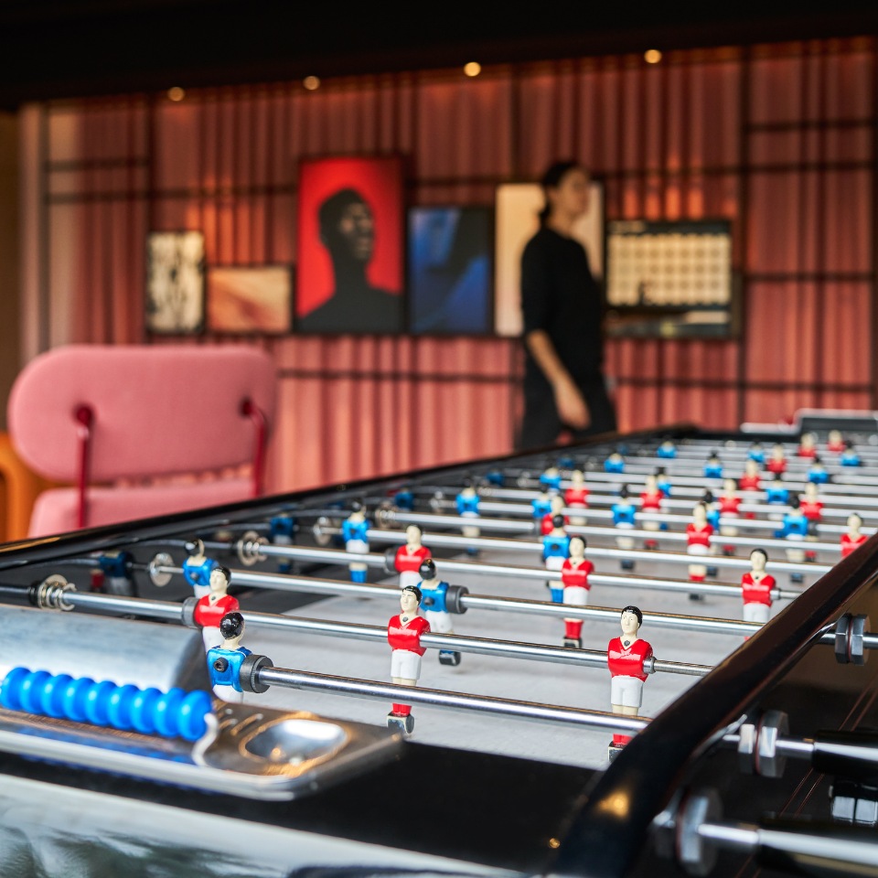 Table football in a lounge with pink seating and framed artwork.