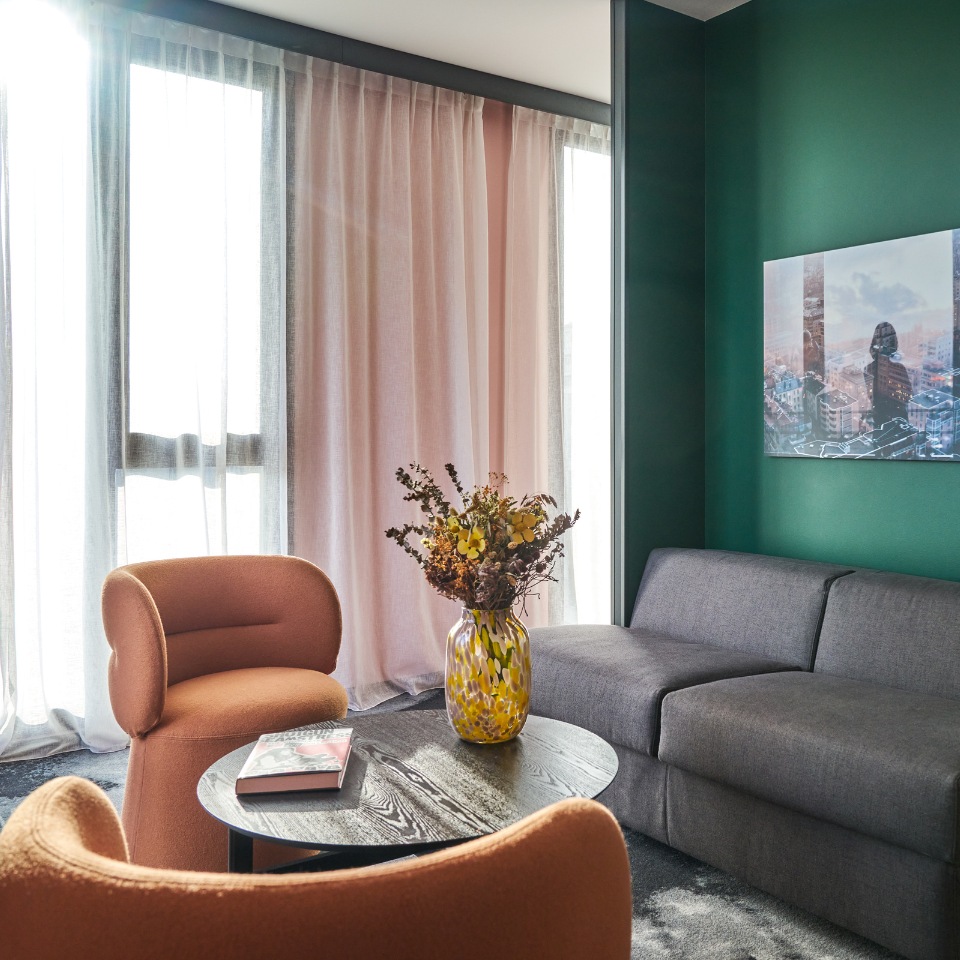 Grey sofa and orange armchairs around a round table beside tall windows.