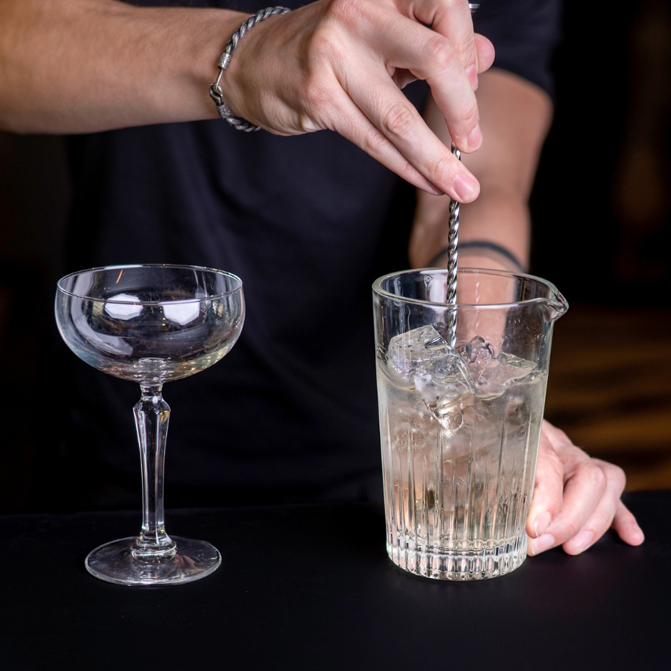 A bartender stirs a drink in a mixing glass.