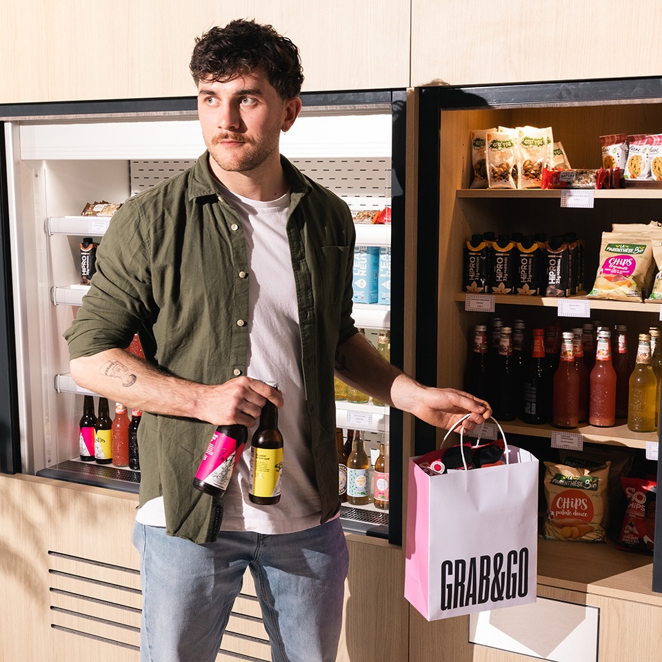 A guest holds a bottle and a Grab & Go bag beside a snack display.