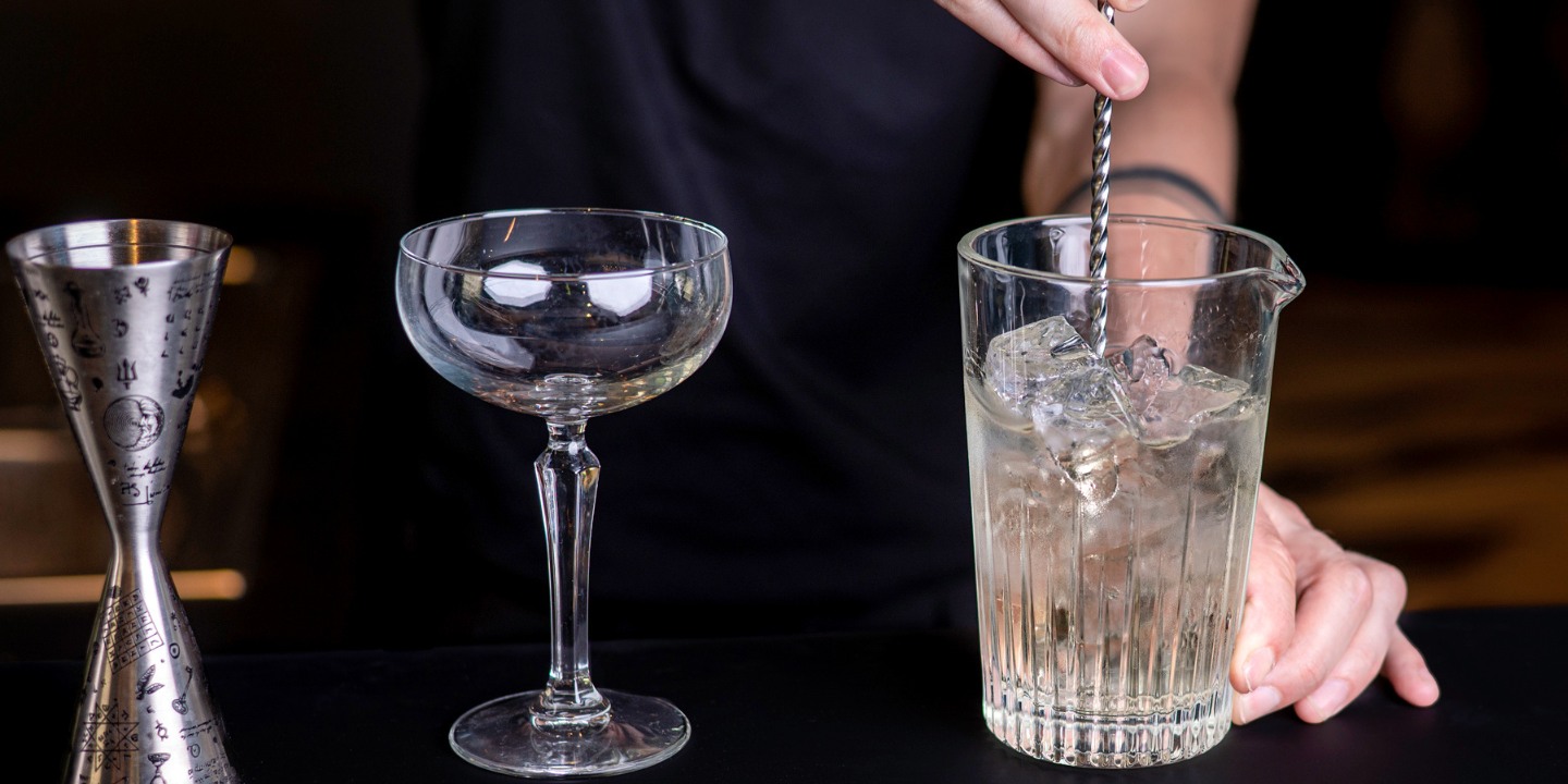 A bartender stirs a drink in a mixing glass.