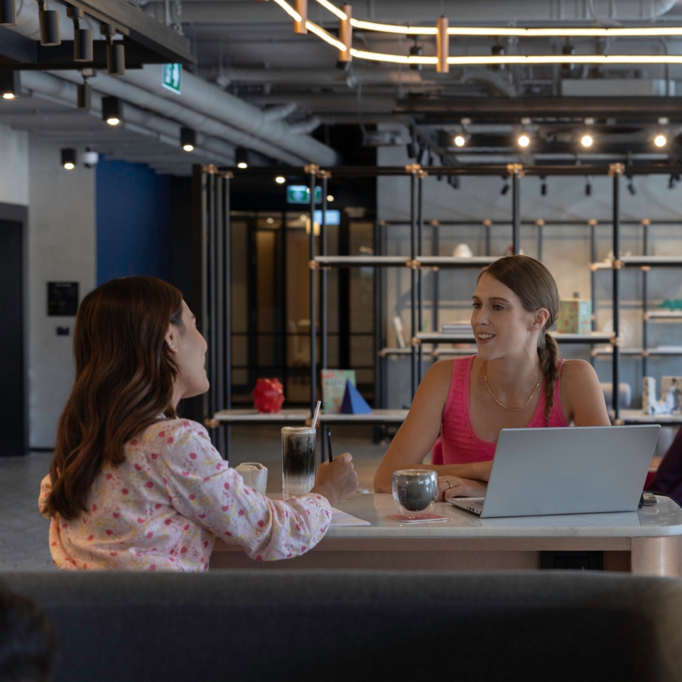 Two people talk beside a laptop at a lounge table.