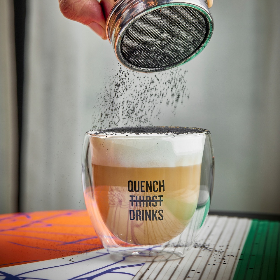 A hand sprinkles powder over a foamy coffee.