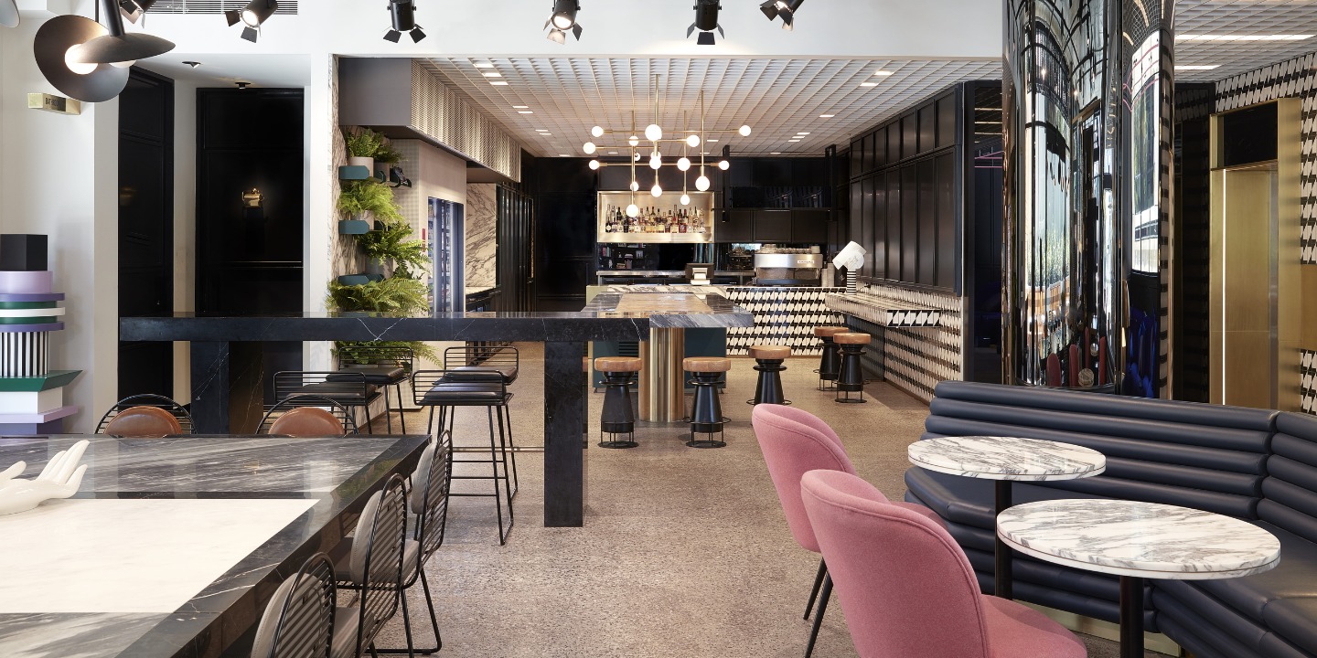 Restaurant with bar, round tables and pink and grey seating.