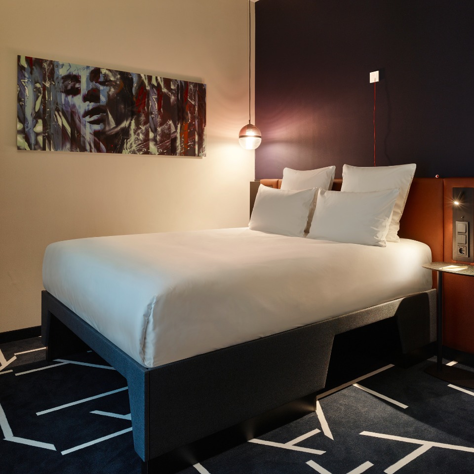 Cozy bedroom featuring a double bed with white linens, modern artwork, and stylish decor against a dark wall.