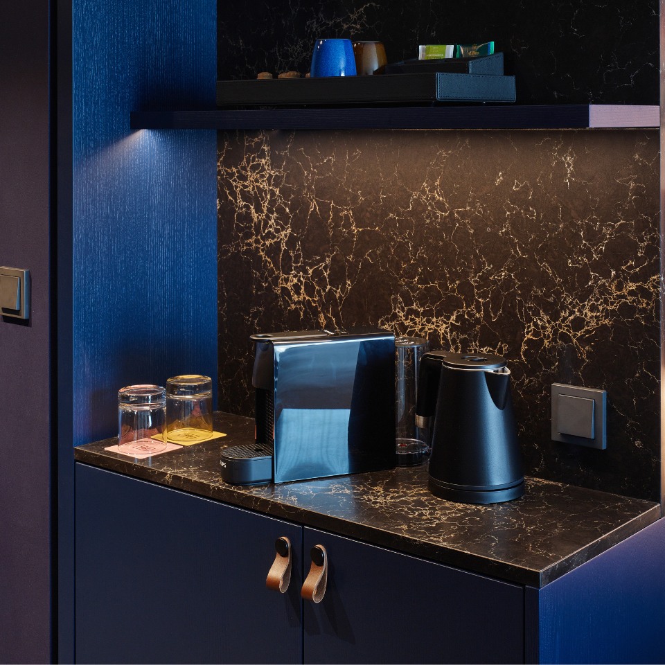 Stylish kitchen nook with a marble countertop, a black kettle, a sleek toaster, glass jars, and blue accents against a dark backdrop.