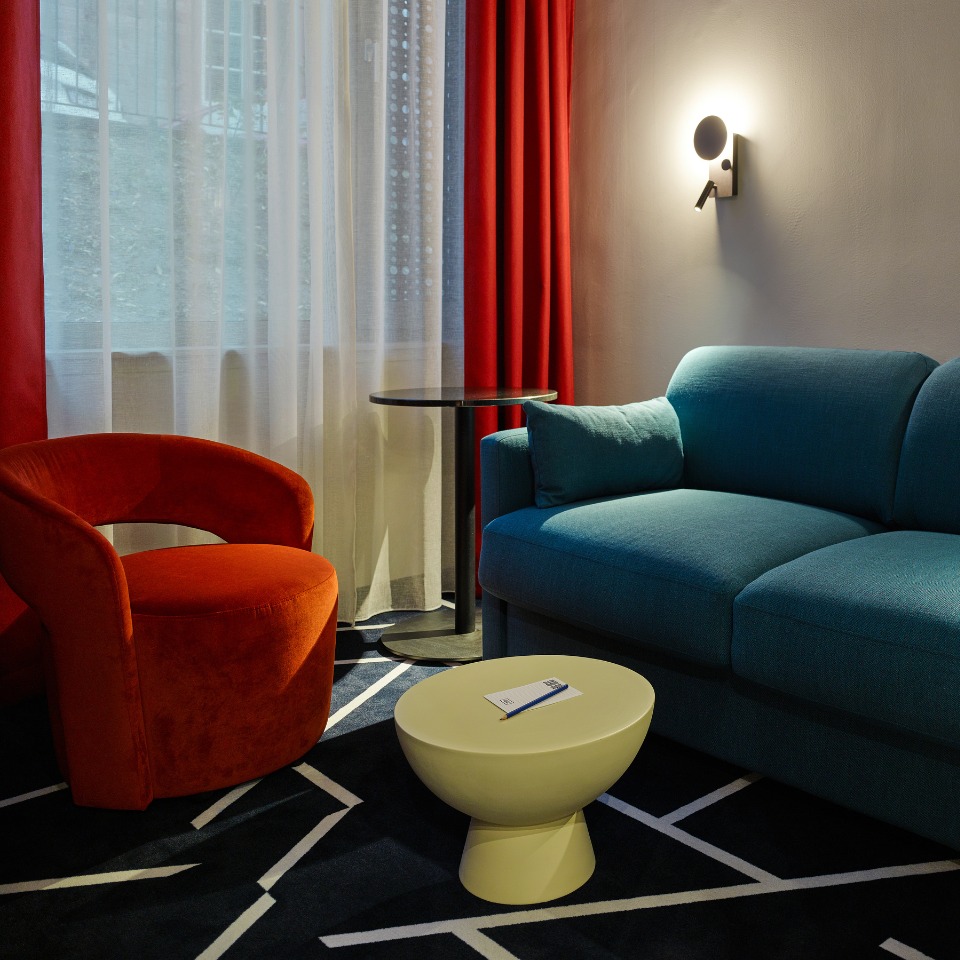Stylish living area featuring a blue couch, red accent chair, round yellow coffee table, and vibrant curtains, creating a cozy atmosphere.