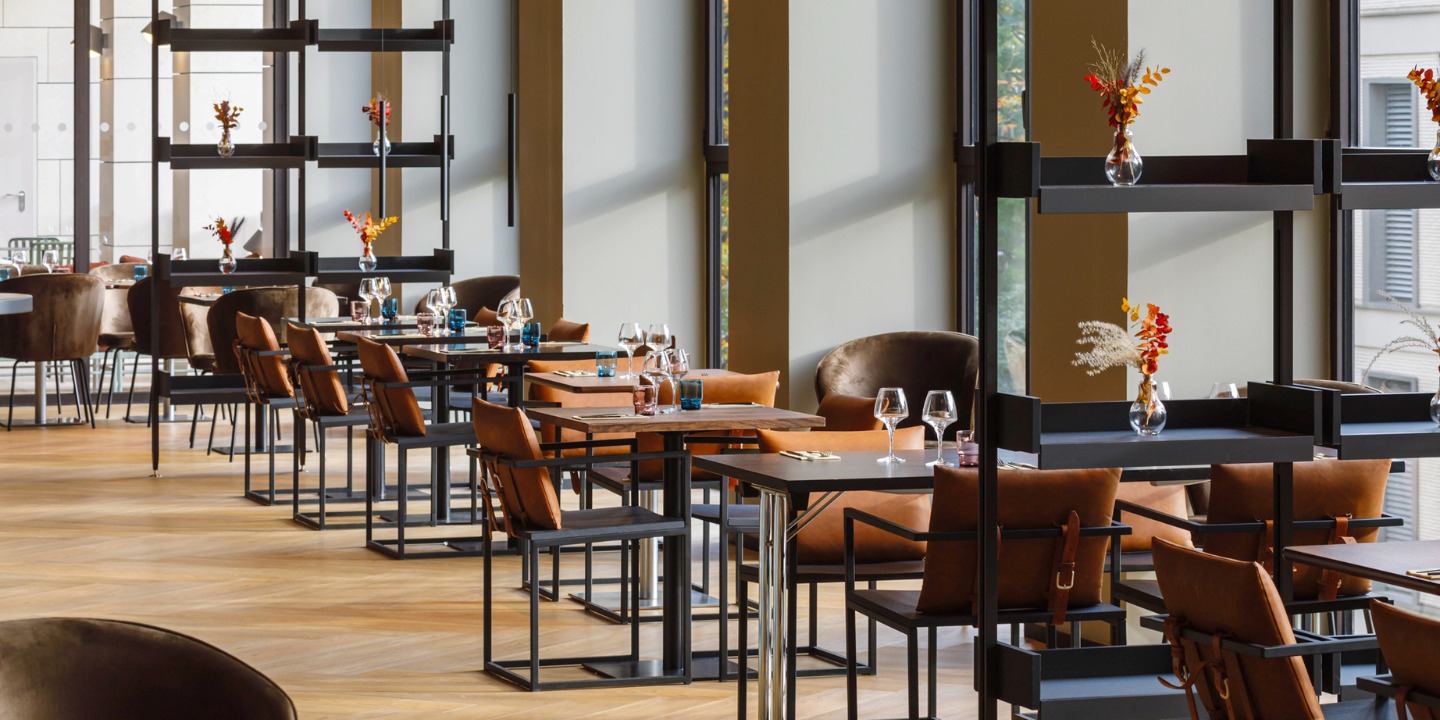 view into the restaurant with chairs with orange cushions and square tables, on the tables are glasses