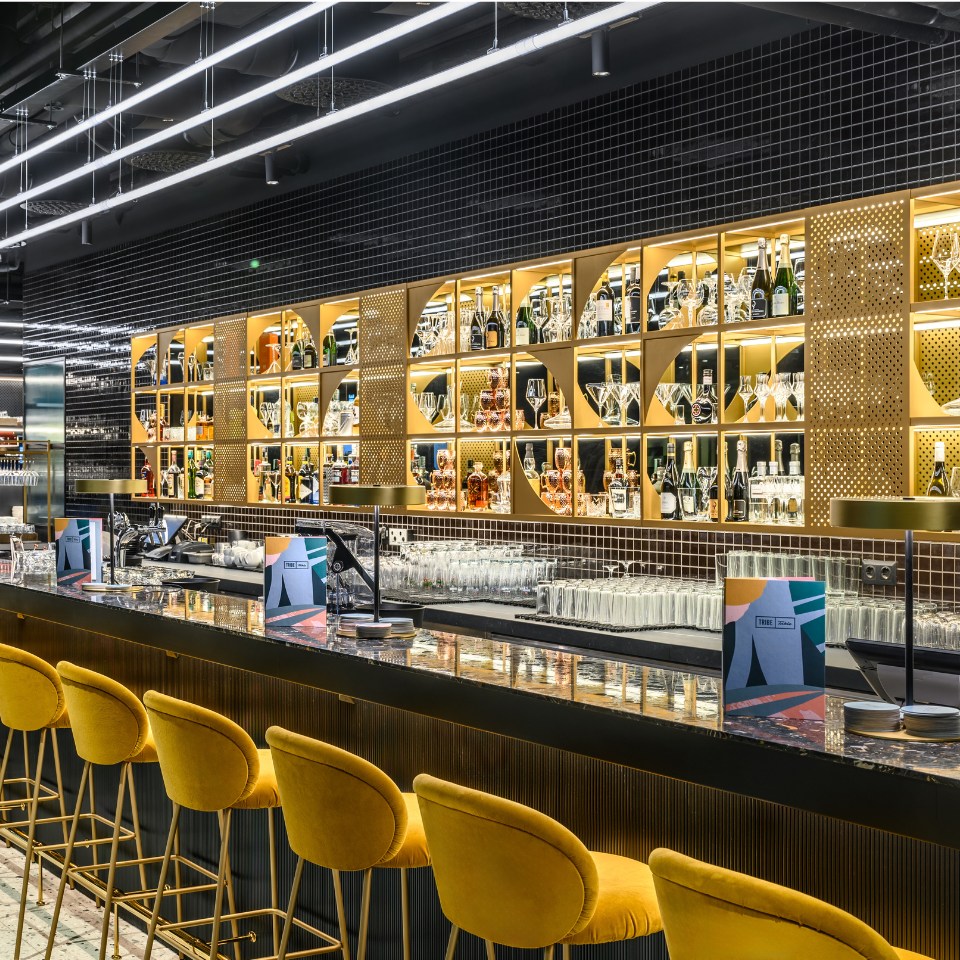 Stylish bar with a modern design, featuring a gold-lit display of liquor bottles and yellow upholstered stools along a polished countertop.