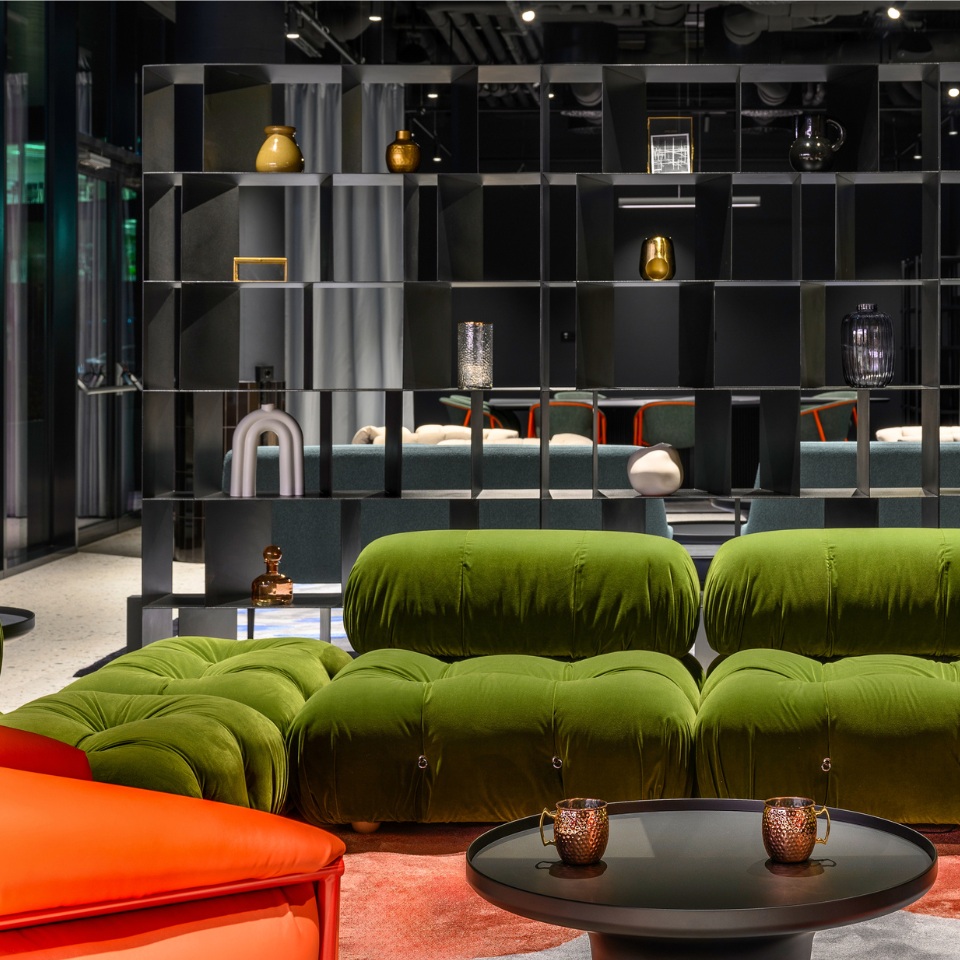 Modern lounge featuring vibrant green and orange sofas, a black bookshelf, and elegant decor, creating a stylish and inviting atmosphere.
