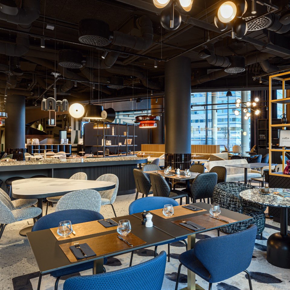 Modern restaurant interior featuring stylish furniture, a marble bar, sleek lighting, and large windows revealing a city view.